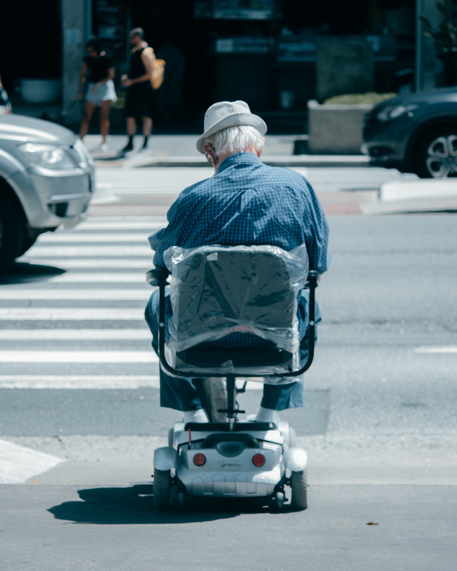 A senior man with a hat and sunglasses is sitting on a mobility scooter while holding a walking stick, with a happy expression on his face.